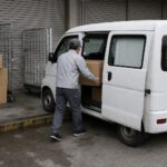 軽バンに荷物を積み込む配達員の後ろ姿