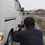 路肩の軽バンの傷を撮影する作業着の人